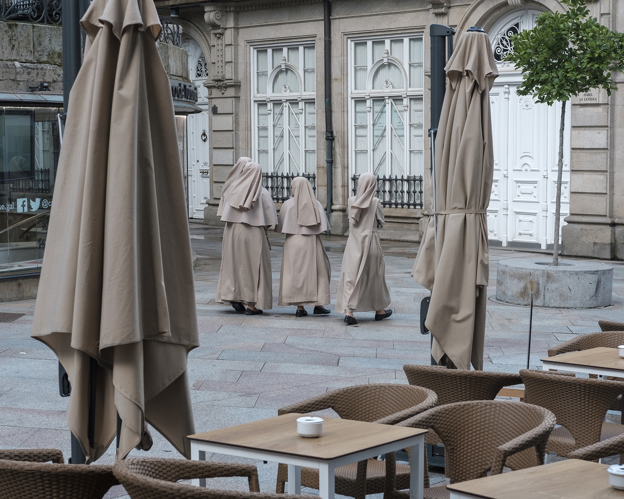 Nuns walk down the street matching the colour and texture of the canopies in the adjacent cafe